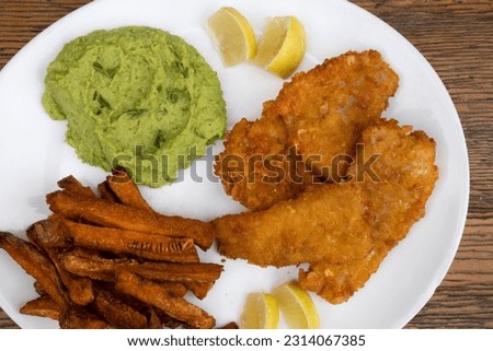 Top view of fried hake fillet with lemon, fried sweet potatoes and beans puree in a white plate with a wooden background.