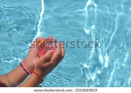 Baby girl play toy in swimming pool on a hot summer day. Kids learn to swim. Child hold balls in water toys. Children play in tropical resorts. Family beach vacation.