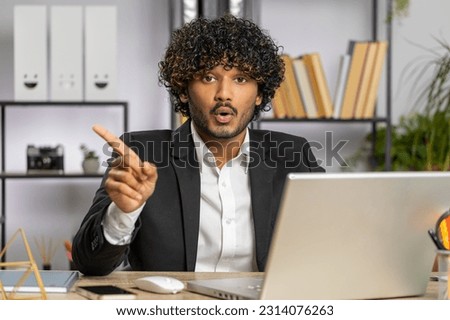 Indian young businessman working on laptop computer shakes finger and saying No be careful scolding and giving advice to avoid danger mistake disapproval sign at home office. Confident freelancer man