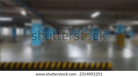 Blurred indoor basement parking area background. Blurred modern underground car park garage with markings, signs, columns and empty parking lots.