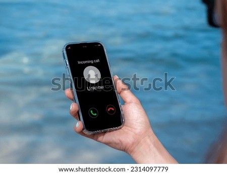 Incoming call with unknown caller, malicious phone calls concept. Unknown number displayed showing on smart mobile phone in woman hand on leave day at the beach. Spam and robocalls, scam call alert. Royalty-Free Stock Photo #2314097779