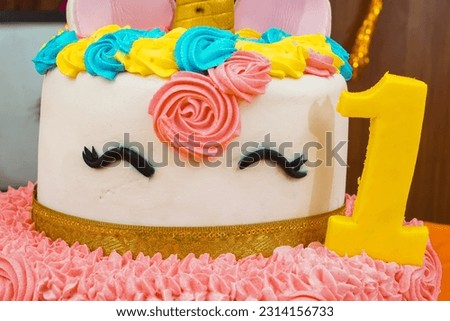 A close-up of a number 1 shaped cake with a swirl of cream and two unicorn eyes. The cream is a light pink color and the eyes are a bright black.