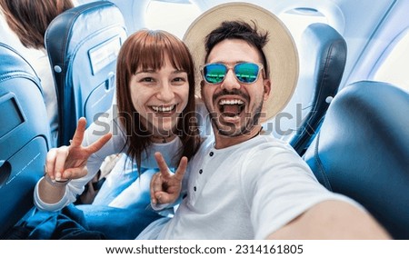 Happy tourist taking selfie inside airplane - Cheerful couple on summer vacation - Passengers boarding on plane - Holidays and transportation concept	

