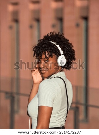 An attractive Latin American teenage girl with curly hair listening to music with white headphones on the street