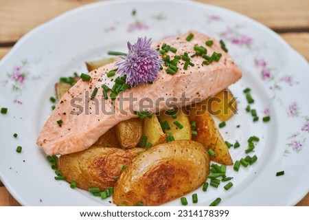 Close up picture on poached salmon with baked new not peeled potatoes and chopped chives served on rustic porcelain plate. Tasty healthy dish, full of nutritions and protein ideal for balanced diet.