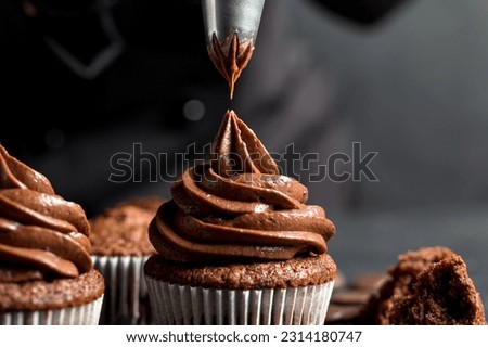 Chocolate cupcakes. The confectioner decorates the cupcake with cream using a pastry bag. Homemade baking concept. Soft focus Royalty-Free Stock Photo #2314180747