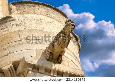 Detail of stone carved gargoyle on a stone tower. View from below. Blue sky, clouds in background.