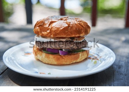 Close up picture on homemade tasty beef burger or hamburger consist from melted and grilled beef from organic farming, sweet bun, spicy sauce, cheese, pickles and vegetables served outside on terrace.