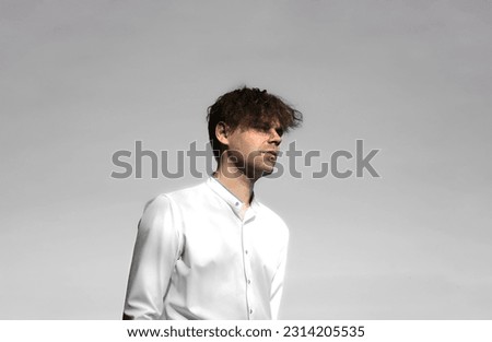 A brutal guy with stubble. A young man in a white shirt on a gray background. Contrast portrait photo.