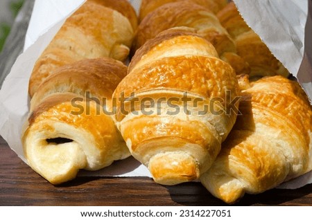 Freshly baked French croissant in a paper envelope in the morning sun. Delicious pastries.