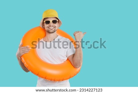 Cheerful man with inflatable circle for swimming on his neck shows copy space on light blue background. Handsome guy in sunglasses, T-shirt and panama with smile advertises summer product. Web banner. Royalty-Free Stock Photo #2314227123