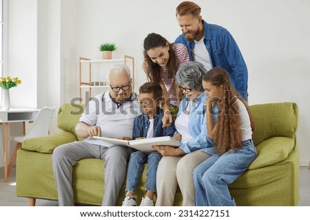Family looks at photo album together and remembers stories from past during reunion of relatives. Elderly couple and their adult children and grandchildren are looking at photo while sitting on sofa.