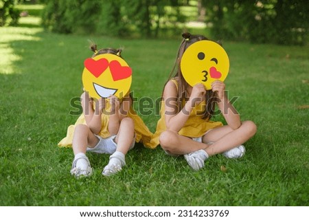 Two girls hide their faces behind the heads of emoticons with different emotions. Loving emojis and blowing kisses Royalty-Free Stock Photo #2314233769