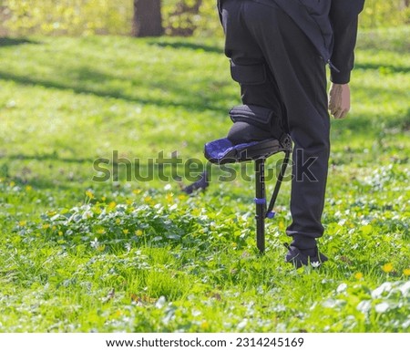 A low-angle view of a young man with a prosthetic leg walking in the park. on a sunny day. A man with a prosthetic leg walks on the green grass in the park, feeds squirrels.