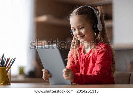 Happy little girl resting at home with digital tablet, cute preteen female child wearing wireless headphones playing online game, happy kid watching videos on modern gadget, copy space