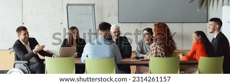 Wide crop photo of a diverse group of business professionals, including an person with a disability, gathered at a modern office for a productive and inclusive meeting. Royalty-Free Stock Photo #2314261157