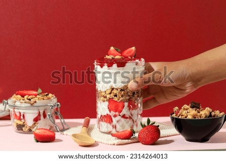 Female Hand Hold Drinking Jar with Strawberry Greek Yoghurt Parfait, Made eith Fresh Fruit, Yoghurt, and Granola. Concept Healthy Eating Diet Menu