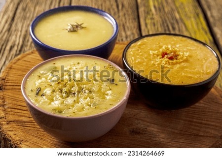 Three delicious hot broths from Brazilian cuisine, cassava, onion and Quenga, served in colorful porcelain pots, with a view from above on a beautiful rustic wooden table typical of a farm