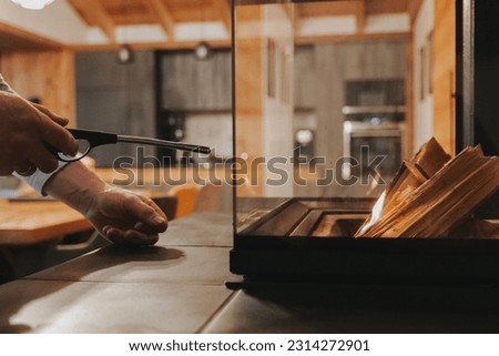 Fire up the fireplace. Glass fireplace in the interior of a cozy wooden chalet.Home fireplace ignition.hands hold a flint and set fire to firewood.