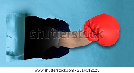 Male fist in boxing glove punching through blue carton paper