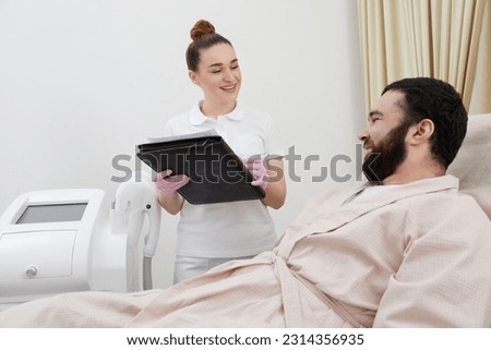 Professional cosmetician woman with papers talking to man before procedure in clinic of esthetic cosmetology