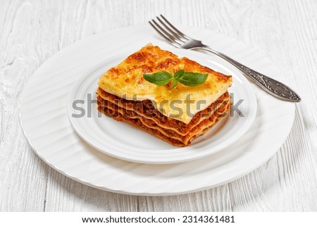 portion of lasagne al forno, italian beef lasagna layered with ground beef, marinara sauce, pasta noodles and ricotta cheese on white plate with fork on white wood table Royalty-Free Stock Photo #2314361481