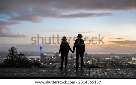 Silhouette image of couple standing on Mt Eden summit and watching sunrise over Auckland city. Selective focus on people in foreground. 