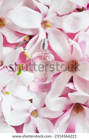 Open bottle of perfume with magnolia flowers, drops of water composition on the pink background. Fresh magnolia aroma. Idea of sweet pure smell of flowers for young girls.