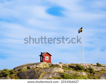 Isolated red swedish wooden cottage and swedish flag on the top of the hill of the island of Vrango in Sweden, near the Gothenburg Royalty-Free Stock Photo #2314366627