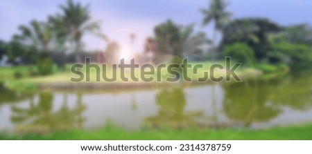 Blurred background of lake in the golf course with palm trees and pines at sunny day. Beautiful golf field with fairway, green, and hole. Nature backdrop, wallpaper concept.