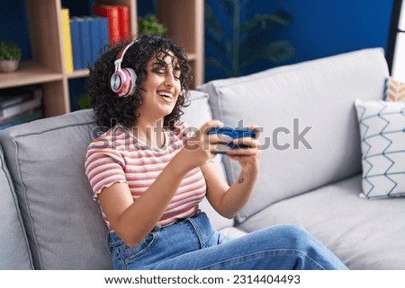 Young middle eastern woman playing video game sitting on sofa at home