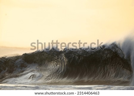 huge shore break wave on a beach at sunset