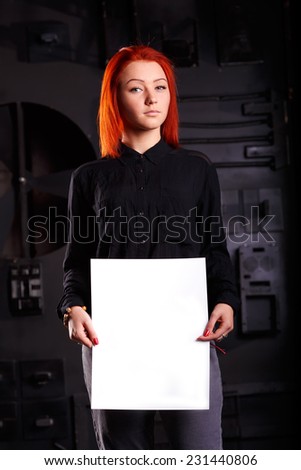 Woman hold blank card, standing on a dark background. Girl holding a large white sheet as the pointer where you can make any inscription. Advertising space that will keep a woman in his hands.