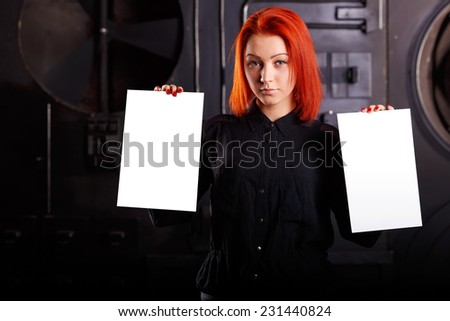Woman hold blank card, standing on a dark background. Girl holding a two large white sheet as the pointer where you can make any inscription. Advertising space that will keep a woman in his hands.