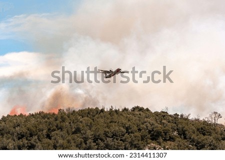 Fire - Airplane dropping fire-retardant product on a forest fire in a mountainous wooded area Royalty-Free Stock Photo #2314411307