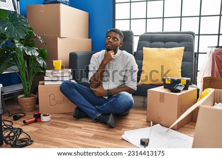 African american man sitting on the floor at new home with hand on chin thinking about question, pensive expression. smiling with thoughtful face. doubt concept. 