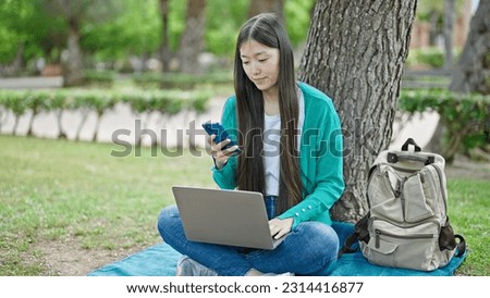 Young chinese woman using laptop and smartphone sitting on floor at park