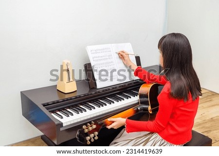 The girl composes songs with a guitar and piano. Royalty-Free Stock Photo #2314419639