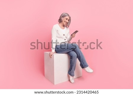 Full size photo of attractive senior woman sitting cube hold device read news wear trendy white clothes isolated on pink color background