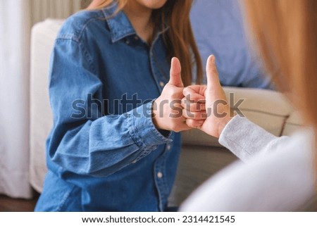 Closeup of a couple women making and showing thumbs up hand sign