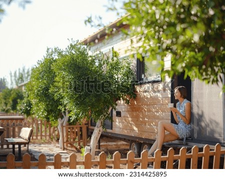 Woman is drinking coffee , morning routine near her Tiny house. First property. Small apartment in summer garden. Minimalism. Moving in. Living alone. Charming trailer house Royalty-Free Stock Photo #2314425895