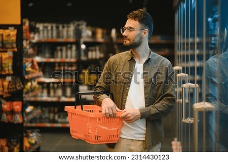 Portrait of smiling handsome man grocery shopping in supermarket, choosing food products from shelf. Royalty-Free Stock Photo #2314430123