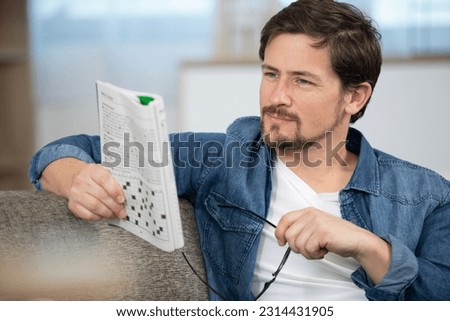 young man sitting doing a crossword puzzle looking thoughtfully Royalty-Free Stock Photo #2314431905