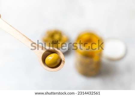 Close-up of olives in a spoon and glass jar on the kitchen table. pitted green olives in jar.Pickled olives in glass jar. On a wooden background.Marinaded olives. Space for text.Space for copy. 
