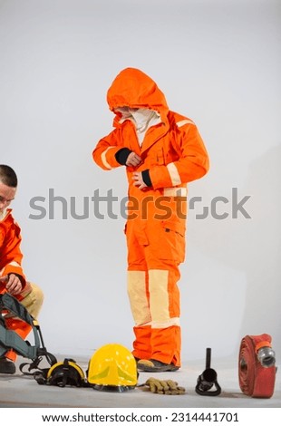 Firefighter is standing zipping up his uniform while a professional firefighter prepares equipment for his partner to wear on white background, Teamwork for work.