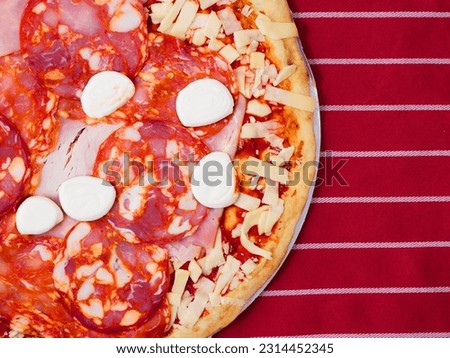 Thin pizza portion with high meat content. Uncooked product with cheese, salami, ham and tomato sous on simple grey red and white stripe table cloth. Dinner preparation. Italian style meal.