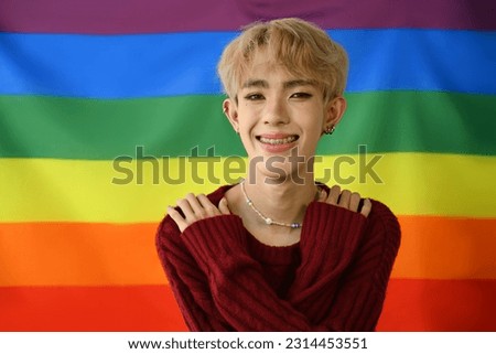 Cheerful homosexual young gay man posing over rainbow pride flag background. LGBTQ, human rights and equality social
