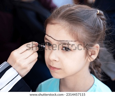 The artist's hand draws on the face of a little girl. Children's holiday