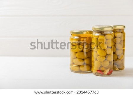 Olives in a glass jar on a white wooden background. pitted green olives in jar.Pickled olives in glass jar. On a wooden background.Marinaded olives. Space for text.Space for copy. Vegan food.