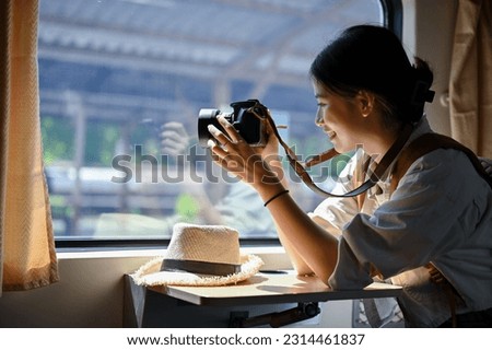 A happy and beautiful young Asian female traveler sits at her seat and takes a picture from the train with her camera. Summer vacation, Journey, Solo traveler